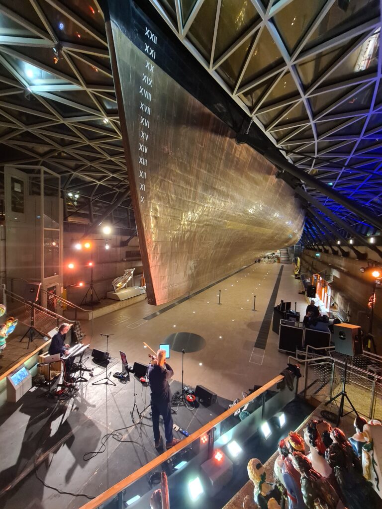 A view of the musicians on stage in front of Cutty Sark, performing site-specific immersive audio.